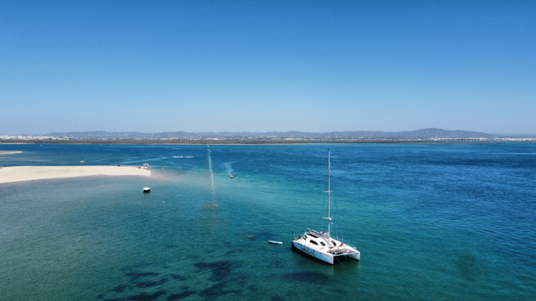 Sailboat anchored in calm blue sea near sandy shore under clear sky.