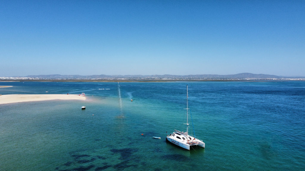 Sailboat anchored in calm blue sea near sandy shore under clear sky.