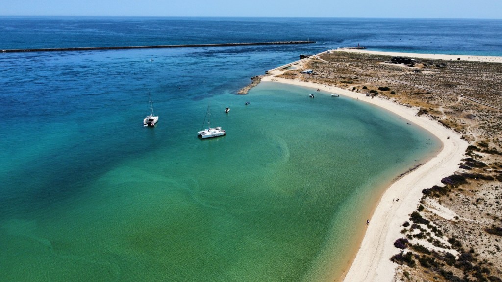 Aerial view of a coastal area with sandy beach and anchored boats in clear turquoise water.