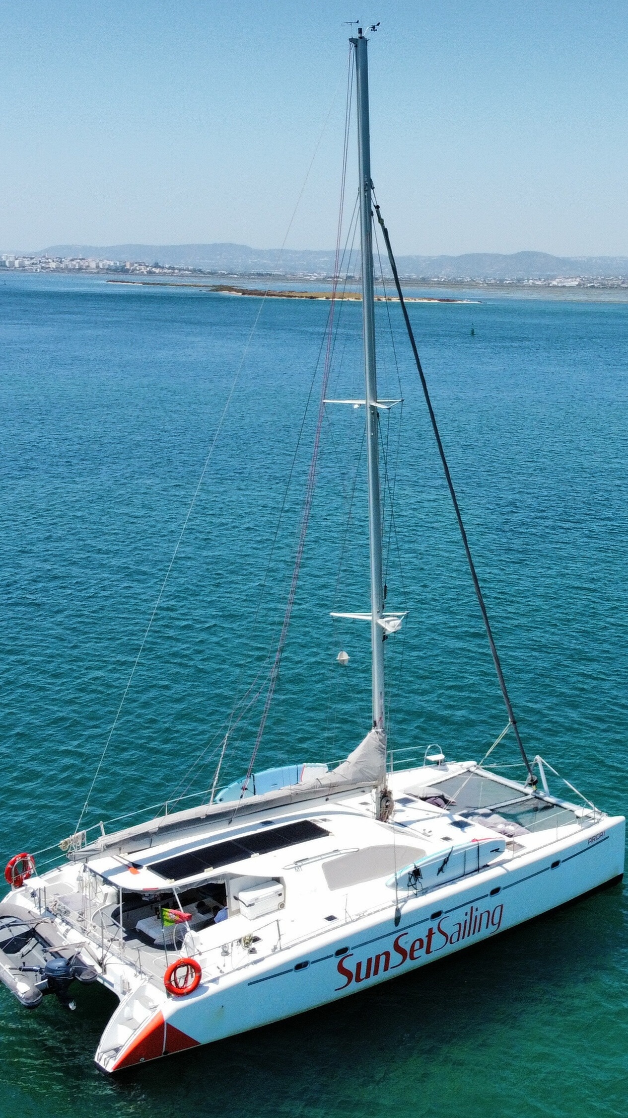 A white catamaran with 'SunSet Sailing' on the side, docked on clear blue water.