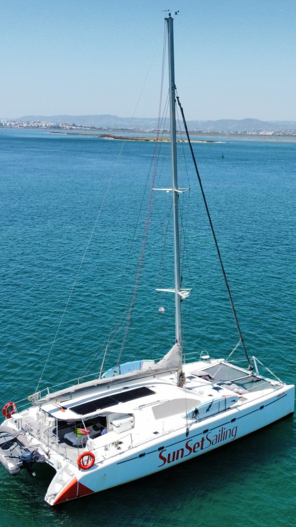 A white catamaran with 'SunSet Sailing' on the side, docked on clear blue water.