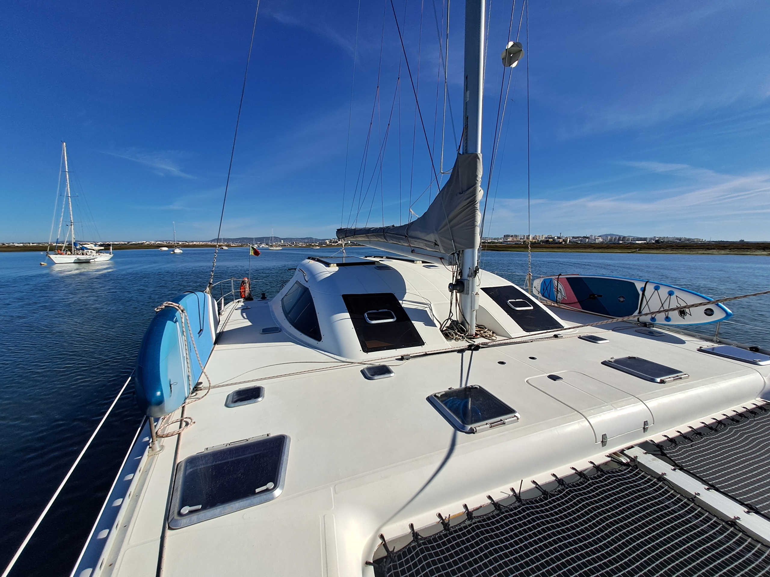 View from sailboat deck with sails down, calm water, and distant boats.