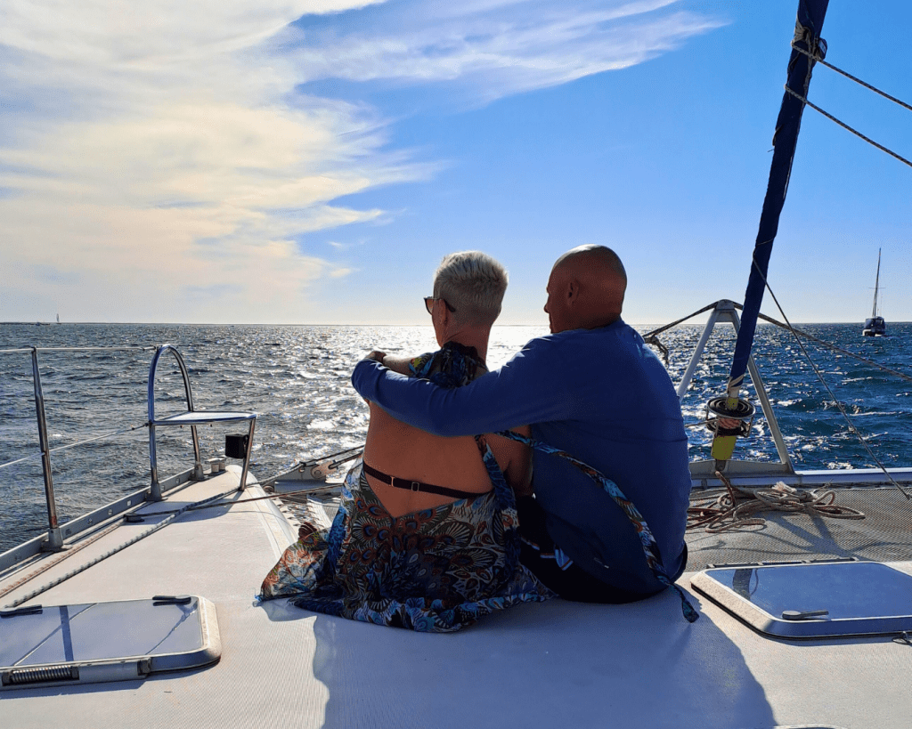 Two people sitting on a boat, looking at the ocean under a blue sky.