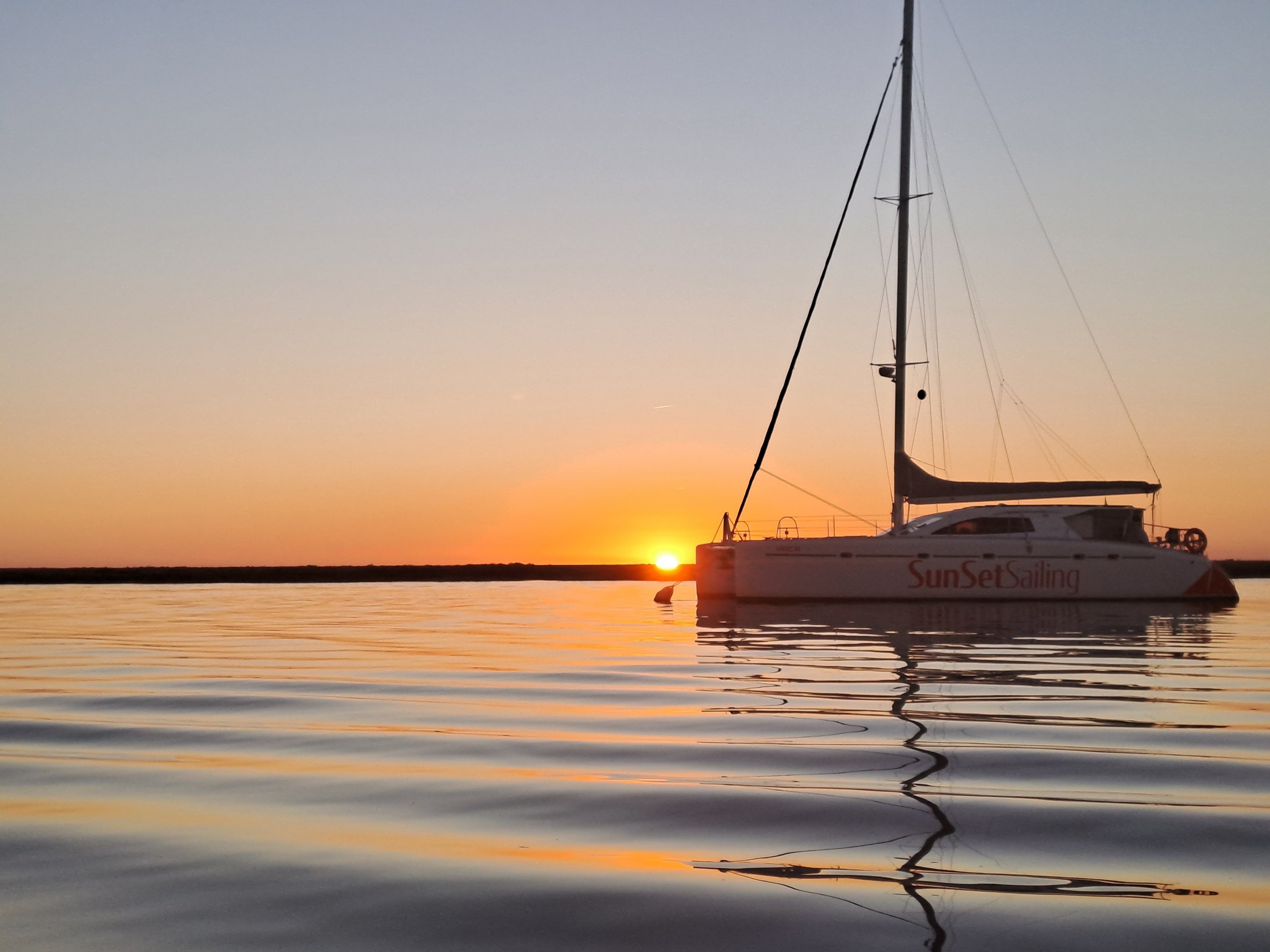 Sailboat on calm water at sunset with orange sky.