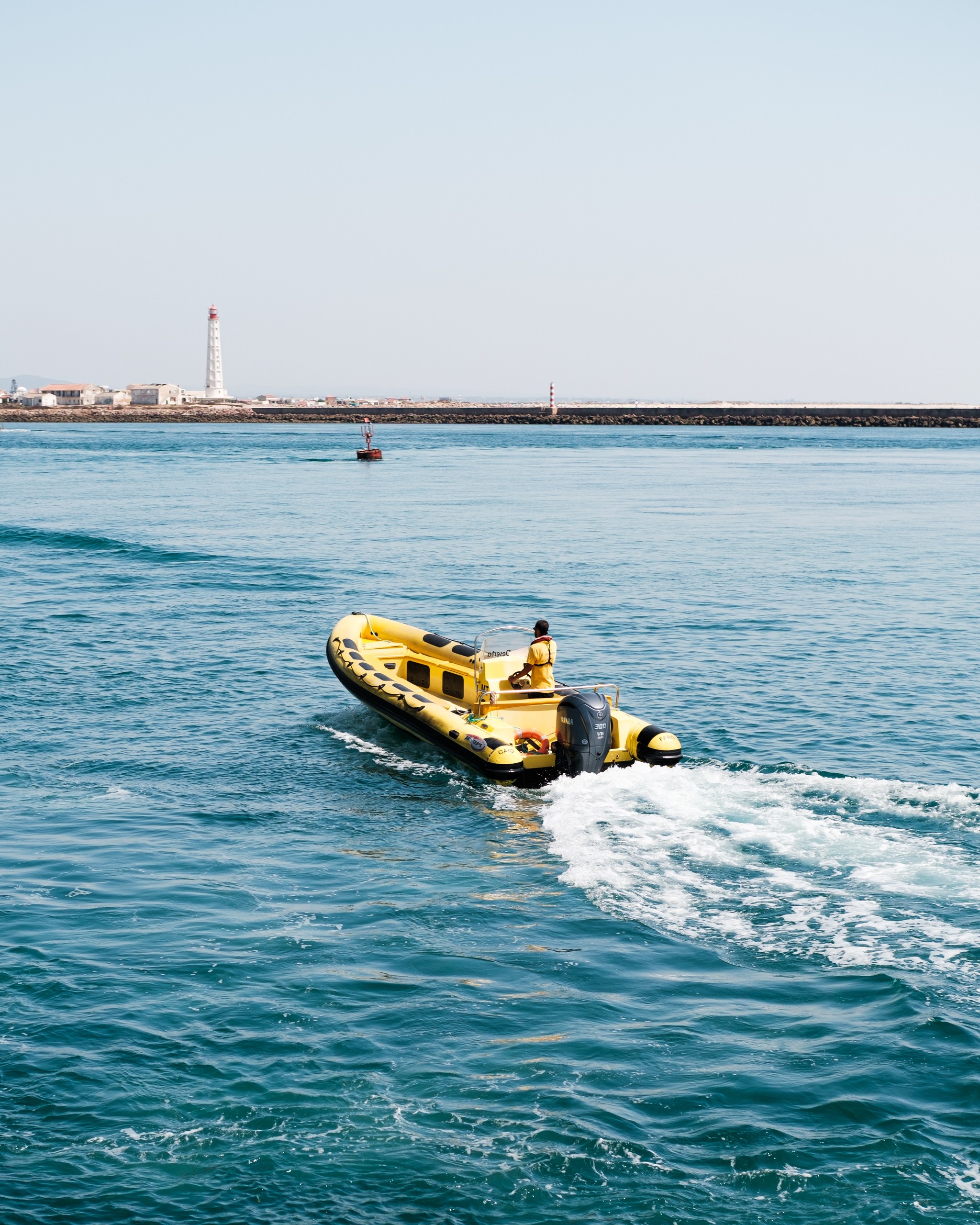Yellow inflatable boat on ocean, lighthouse in background.