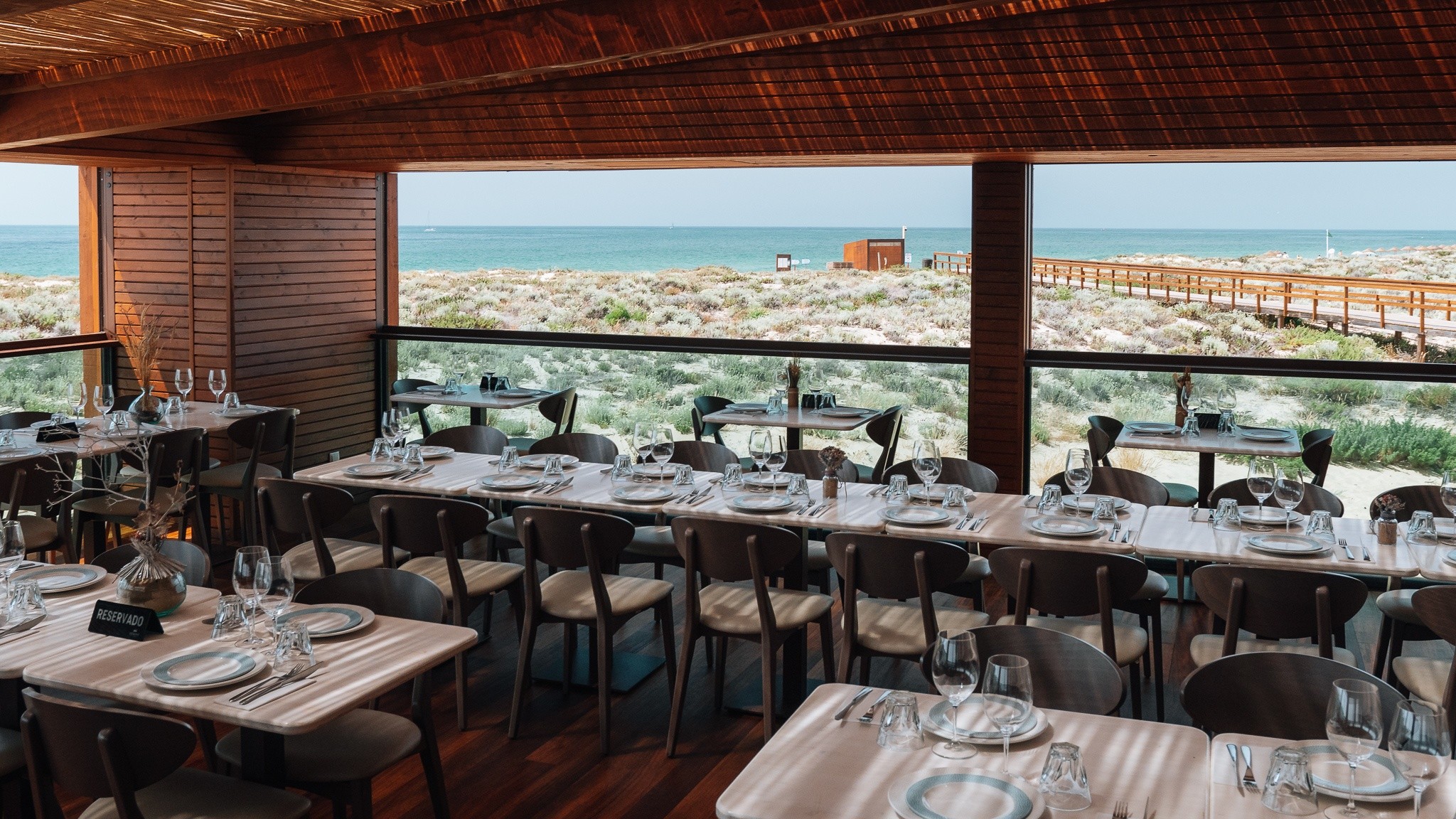 Coastal restaurant with set tables, wooden interior, and ocean view.