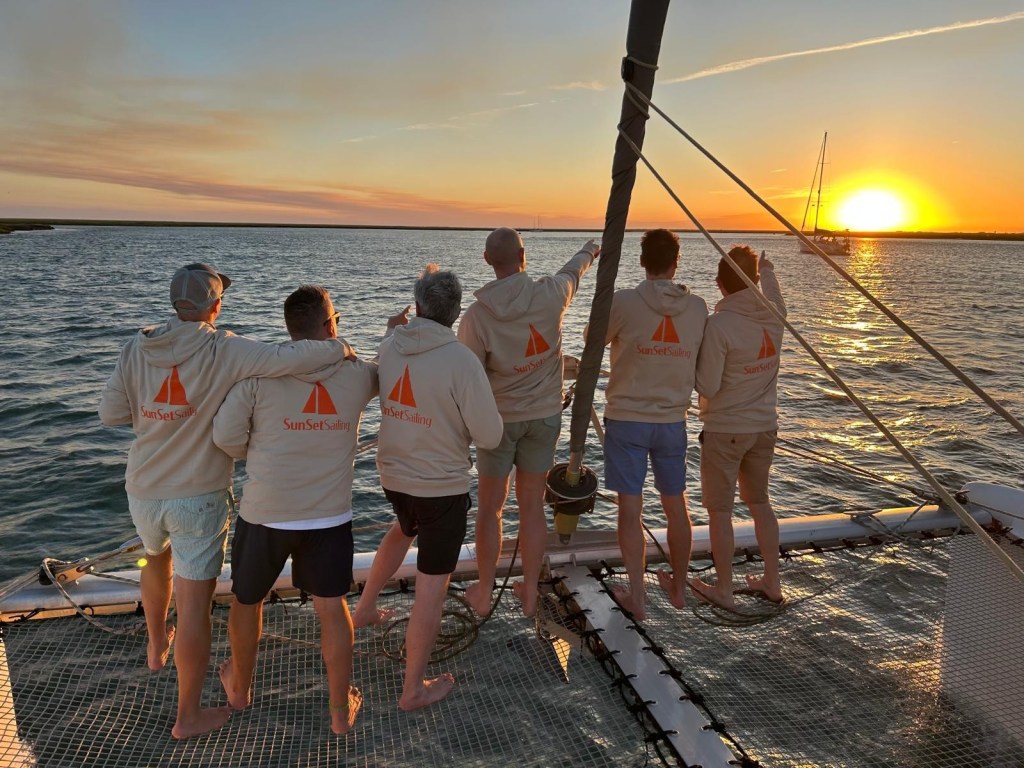 Six people on a boat watching a sunset, wearing matching jackets.