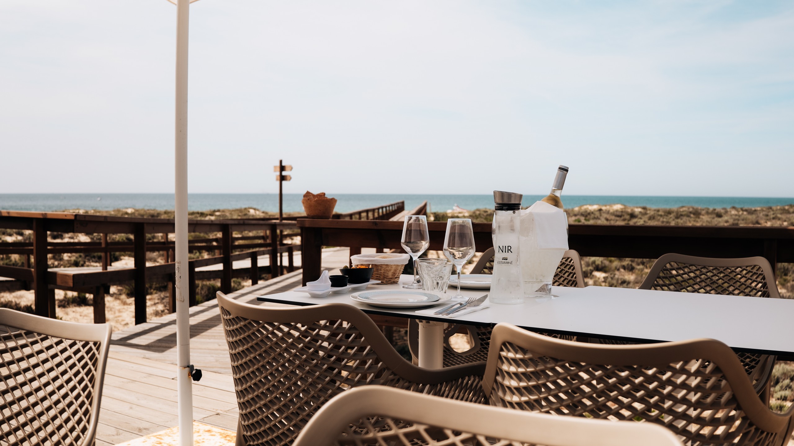 Outdoor table by the beach with wine, glasses, and wicker chairs.