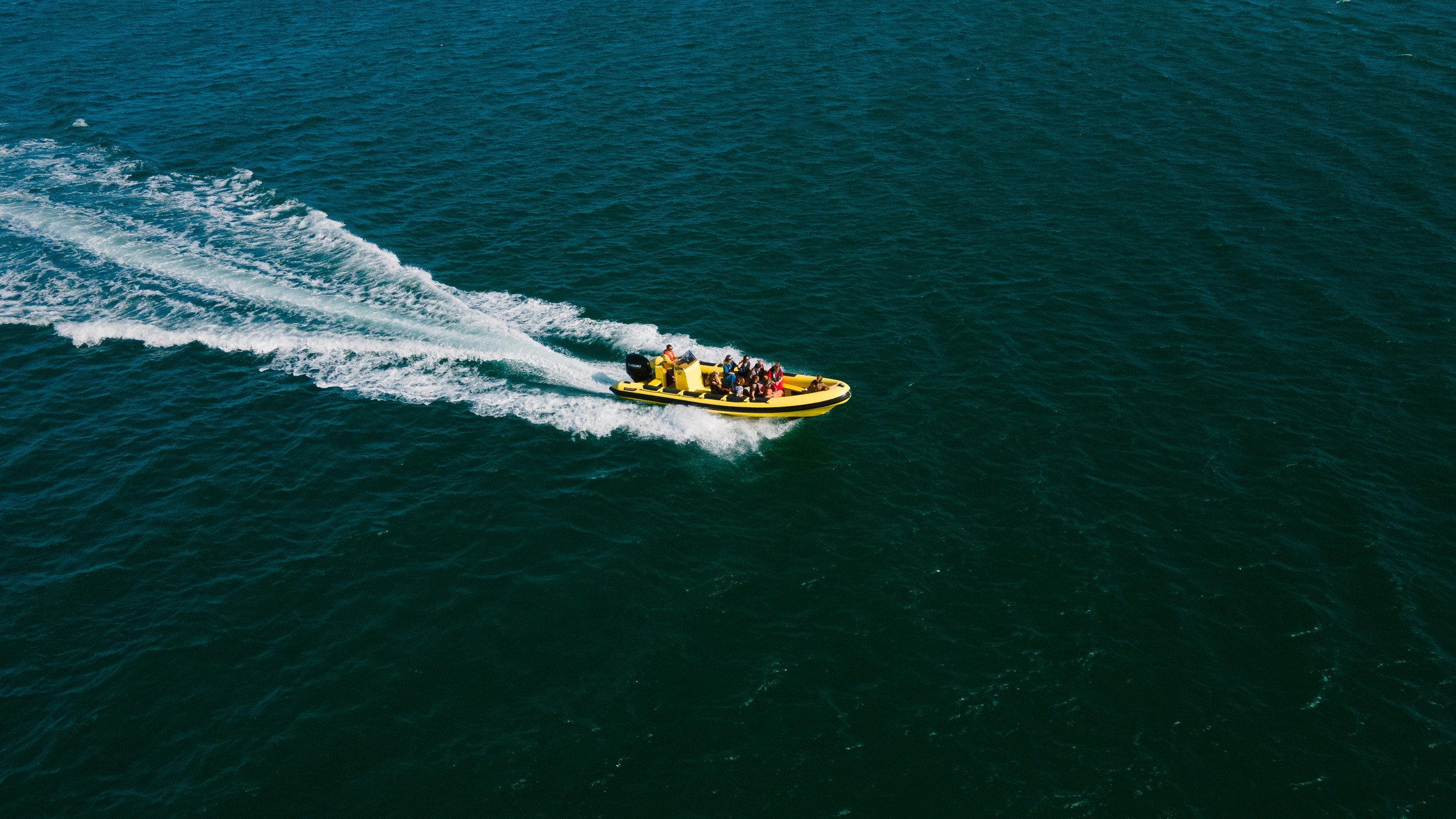 Yellow speedboat with passengers creates wake on open water.