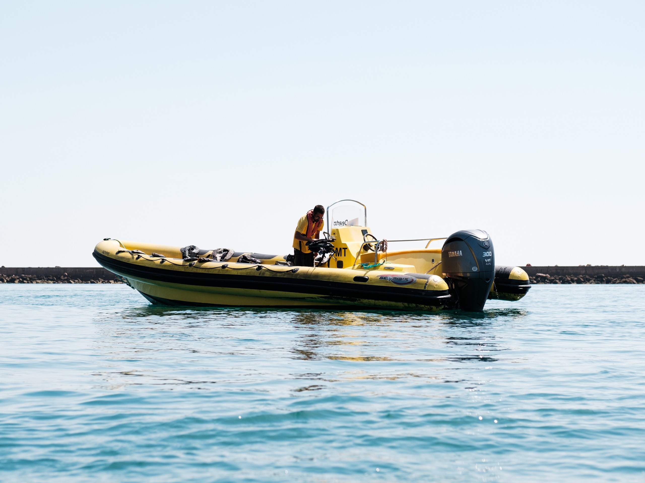 Person in a yellow inflatable boat on calm water, under a clear sky.