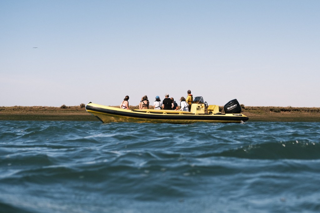 People on a yellow inflatable boat on water with a shoreline in the background.