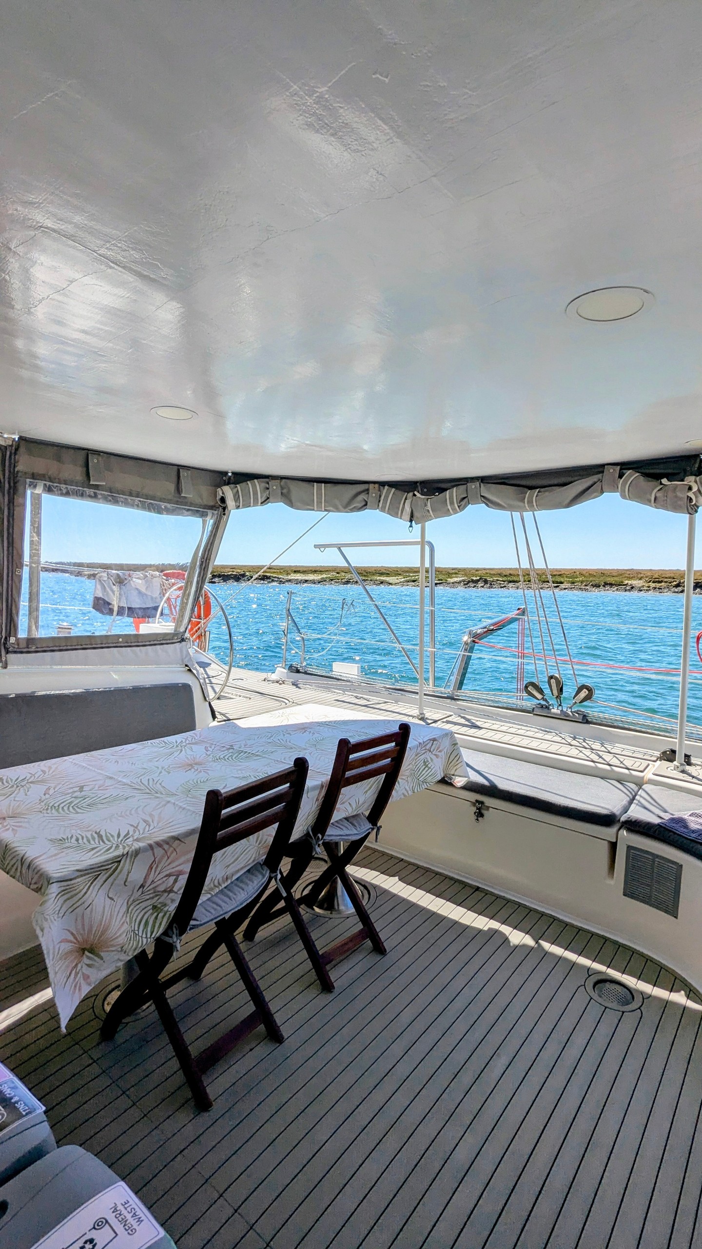 Covered boat deck with table and chairs overlooking calm blue water.