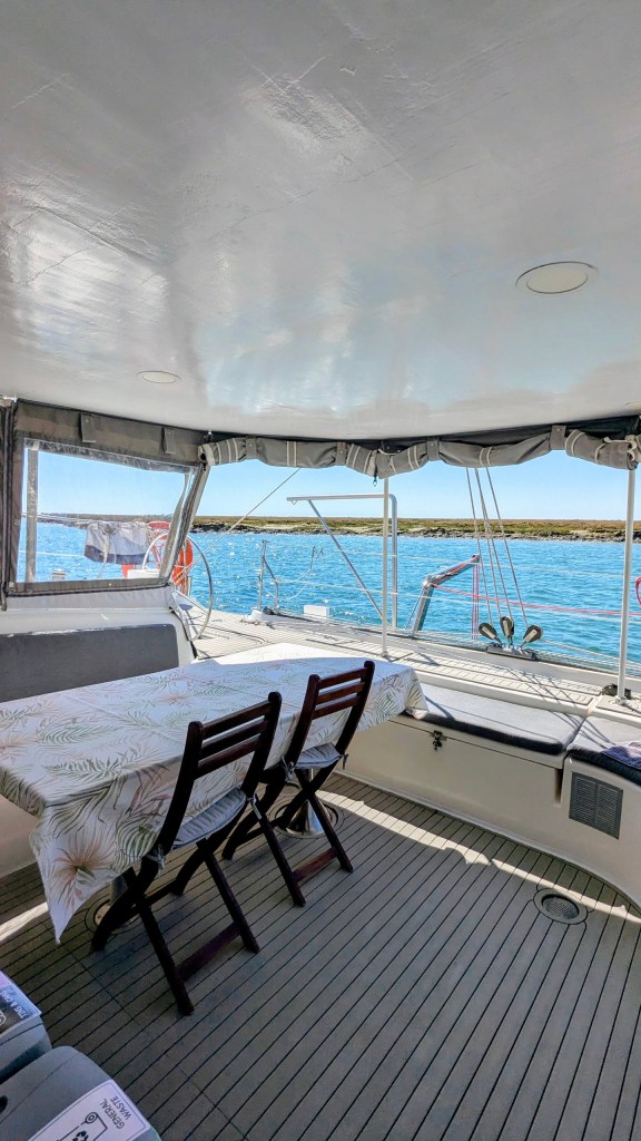 Covered boat deck with table and chairs overlooking calm blue water.