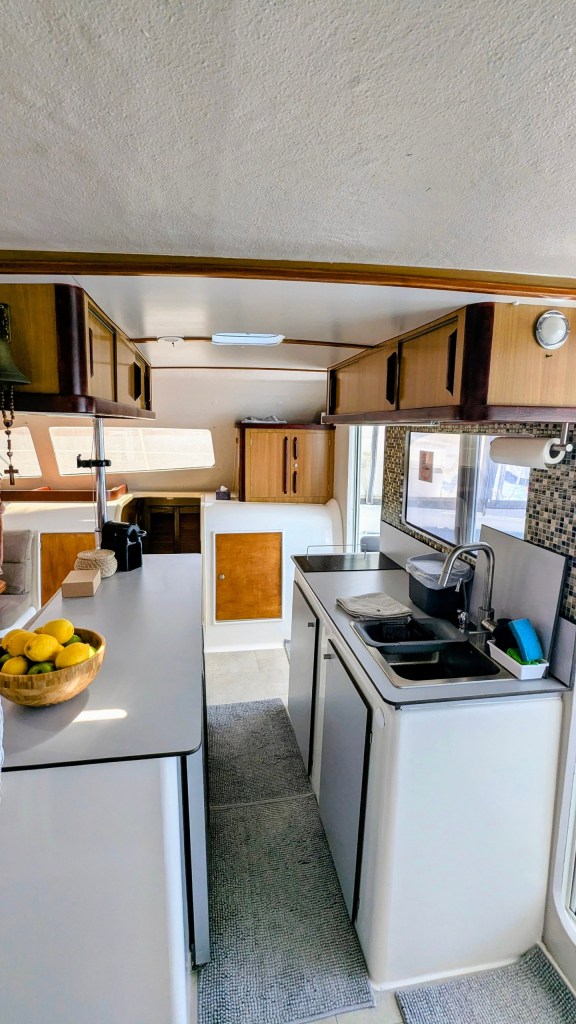Compact kitchen in an RV with sink, stove, fridge, and fruit bowl.