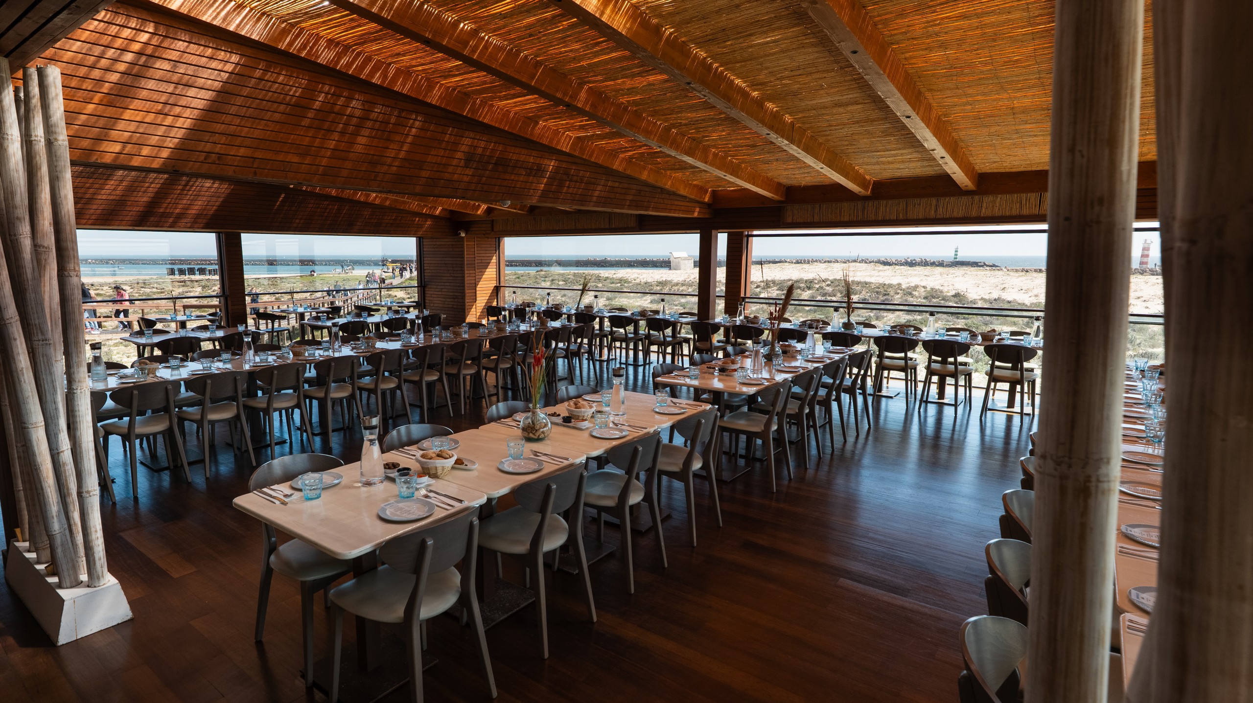 Spacious restaurant with wooden roof, tables set for dining, and large windows overlooking the beach.
