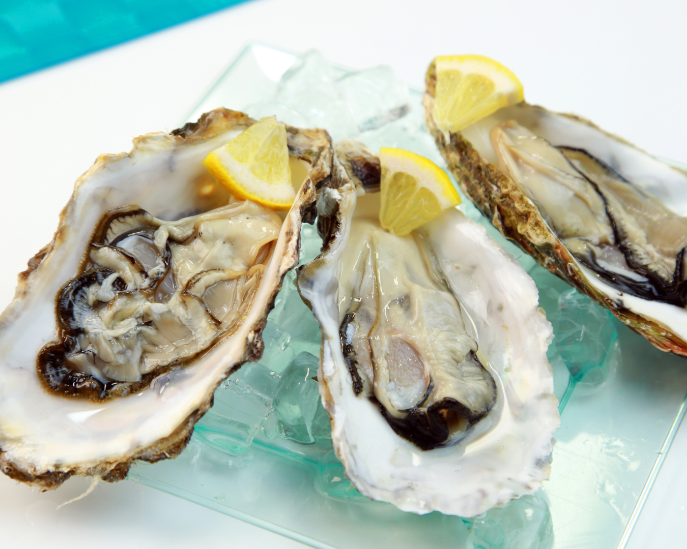 Three oysters on ice with lemon wedges on a clear plate.