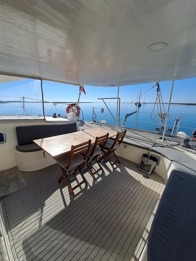 Outdoor seating area on a boat with table, chairs, and ocean view.