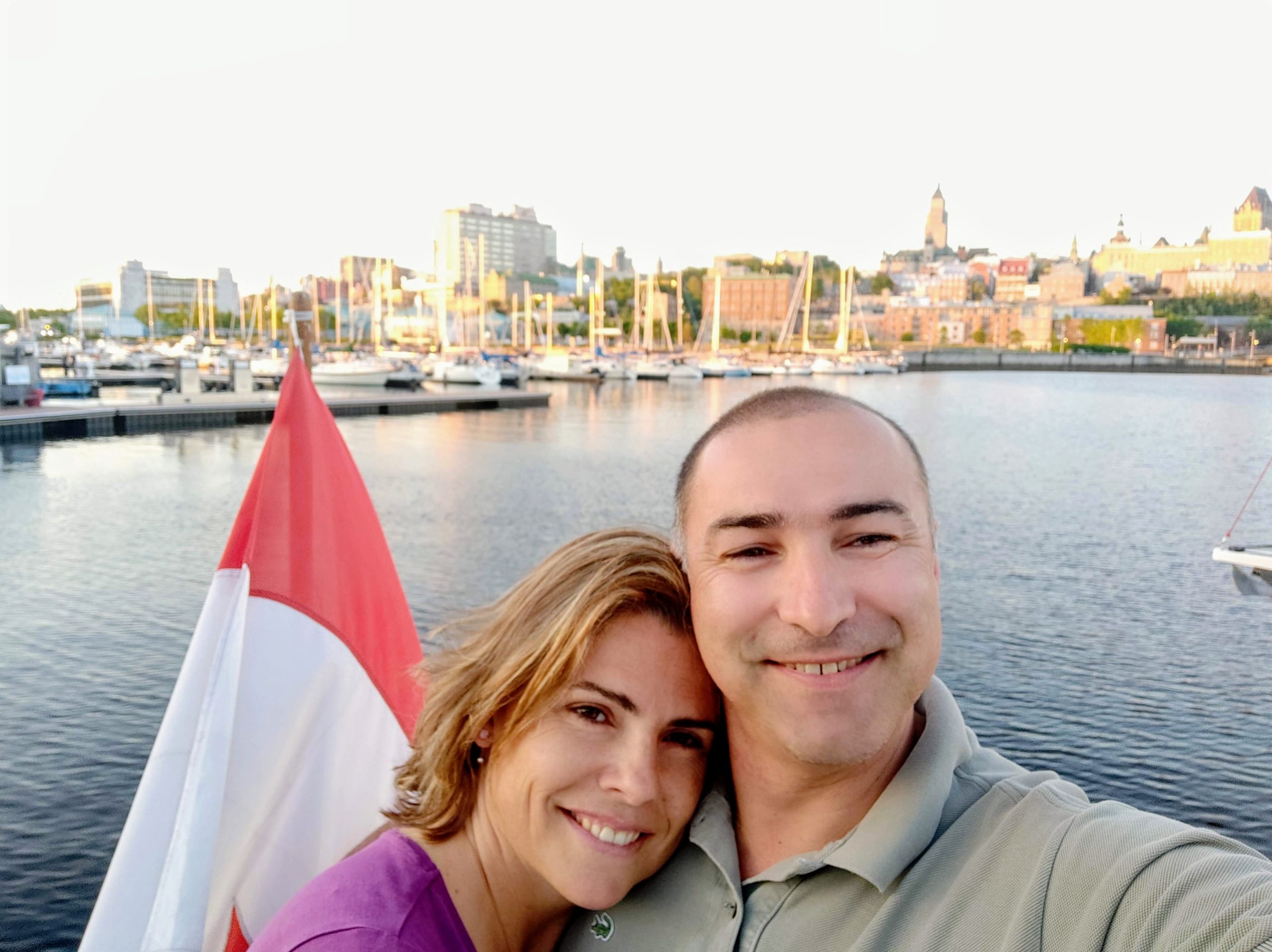 Smiling couple on a boat with cityscape and marina in the background.