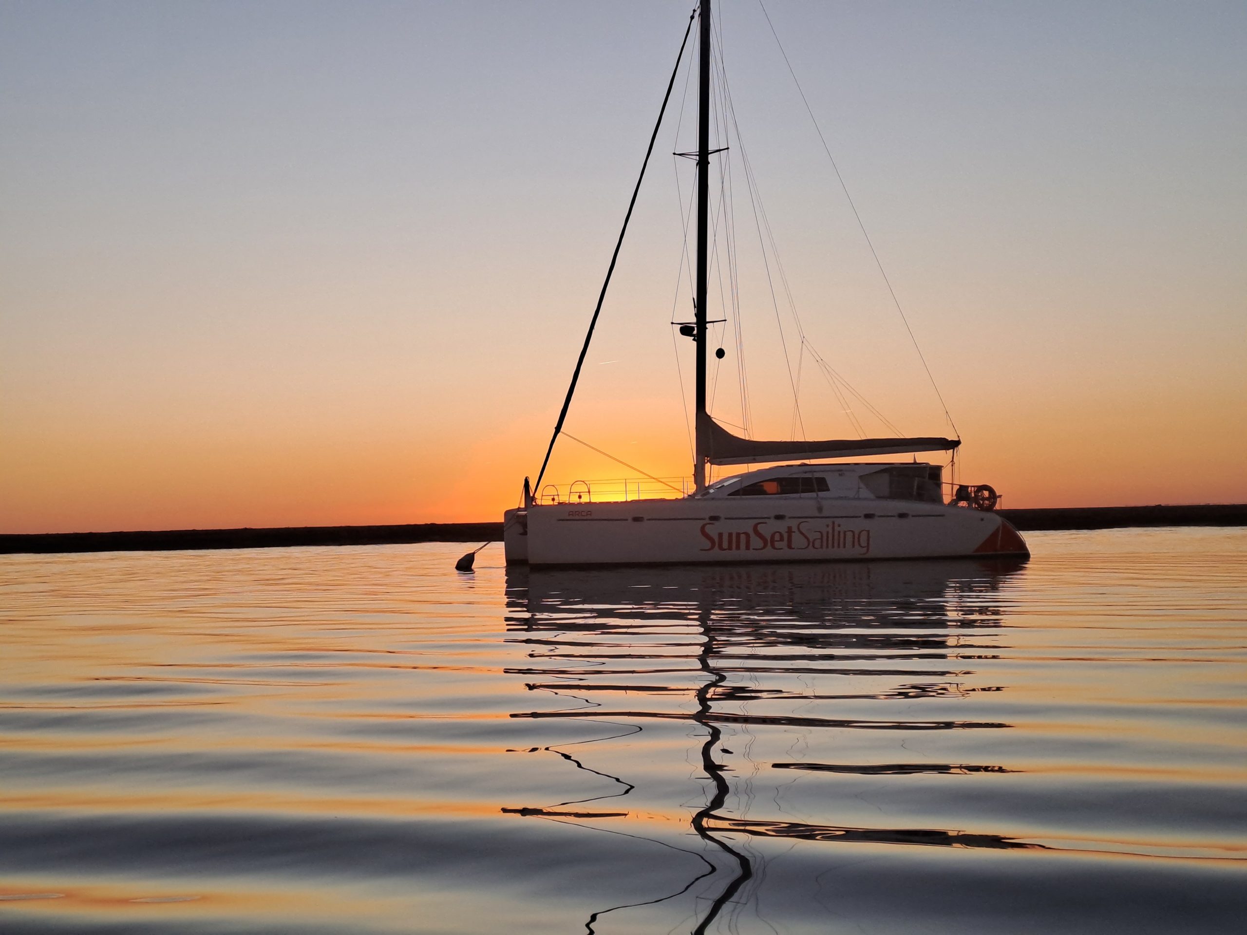 Sailboat on calm water at sunset with an orange sky.