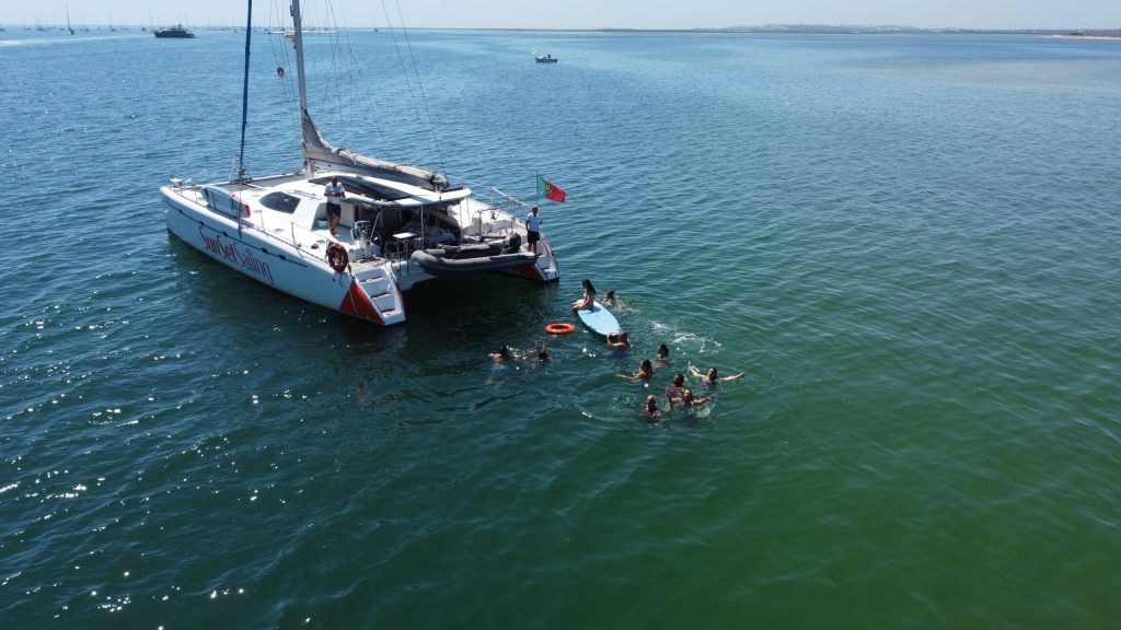 Catamaran in ocean with people swimming nearby on a sunny day.